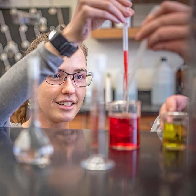 Female student dropping red liquid into beaker