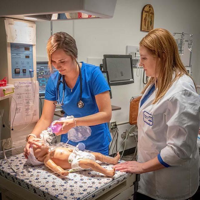 Student nurse giving oxygen to a mannequin of a baby in simulation lab with professor monitoring